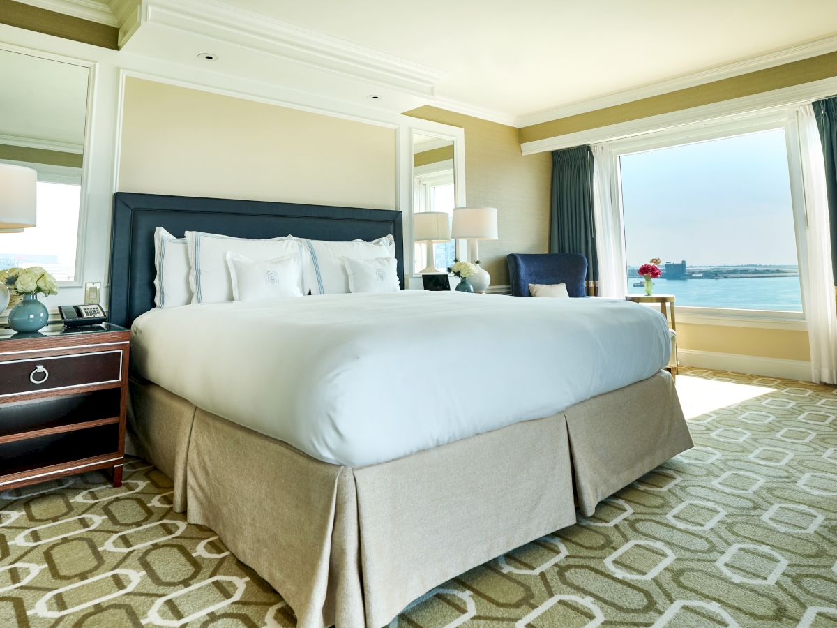 A well-lit hotel room with a large bed, nightstands, and a scenic window view, featuring neutral tones and modern decor.