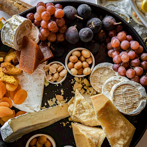 A charcuterie board featuring various cheeses, grapes, dried fruits, nuts, and bread, with oysters and lemon in the background.