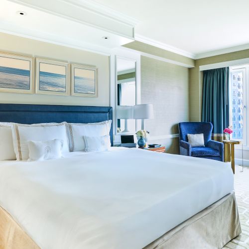 A spacious hotel room with a large bed, windows with city views, and elegant decor, creating a comfortable and inviting atmosphere.