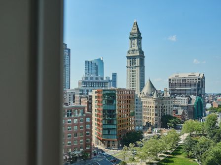 A cityscape featuring a cluster of buildings, with a prominent clock tower and a view of green spaces under a clear blue sky.