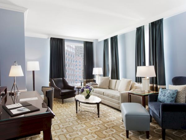 Elegant room with sofa, chairs, desk, lamps, and large windows.