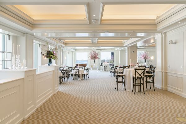 An elegant, spacious event hall with floral arrangements, tables, and soft lighting over a patterned carpet completes the setting.