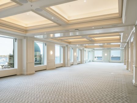 Bright luxury yacht lounge with a coffered ceiling, large harbor-view windows, and built-in benches along white walls.