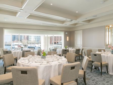 The image shows an elegant banquet room with round tables, each covered with white tablecloths and set for a meal, with floral centerpieces.
