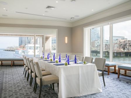 A conference room with a table set for a meeting, overlooking a water view with a docked boat and cityscape in the background.
