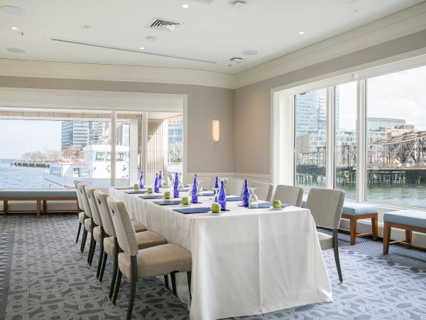 A conference room with a table set for a meeting, overlooking a water view with a docked boat and cityscape in the background.
