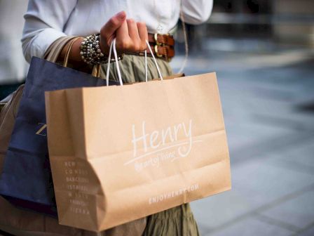 Person carrying a shopping bag labeled "Henry" with blurred background.