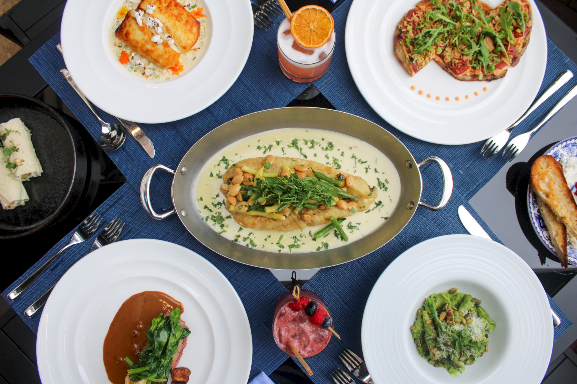 An array of gourmet dishes and drinks on a table, featuring meats, pasta, salads, and cocktails, elegantly presented.