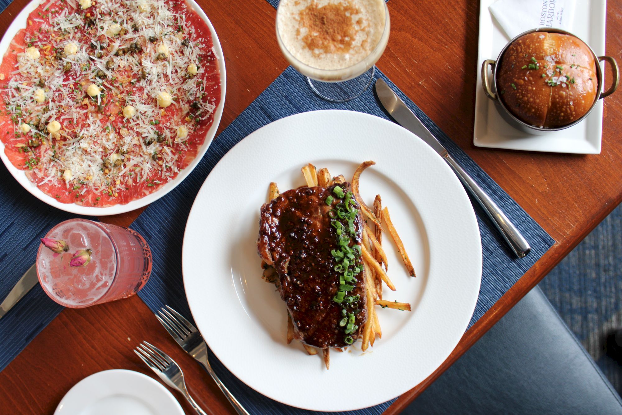 A table spread with a topped pizza, lamb chops with gravy, soup, and drinks for a hearty meal!