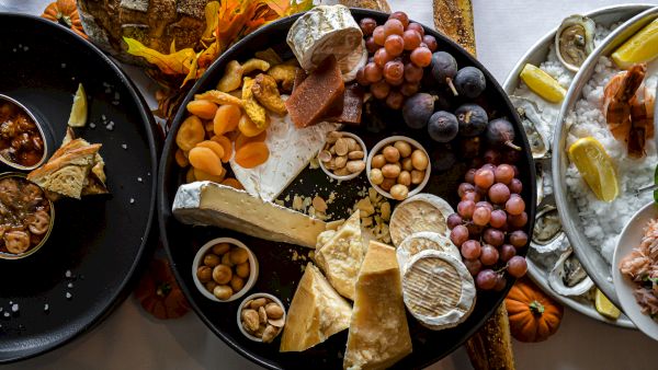 A charcuterie board with cheese, grapes, nuts, dried fruits, and bread arranged artistically on a table.