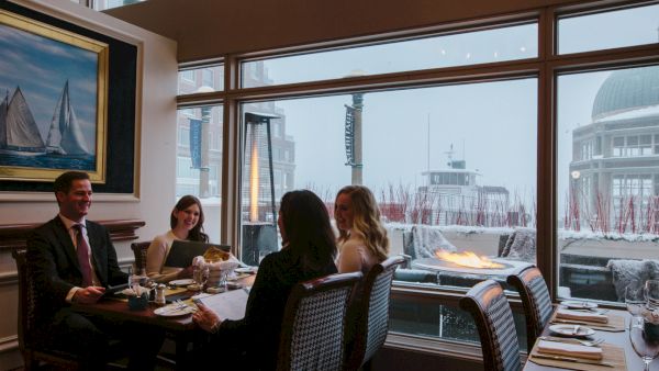 People sitting at a dining table in a restaurant with large windows showing a snowy outdoor scene and a lighthouse visible.