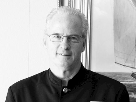 A person in a uniform is standing in front of a framed picture, wearing glasses and a name tag.