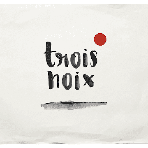 The image shows the words "trois noix" in a black, brushstroke font with a small red circle above the text on a white background.