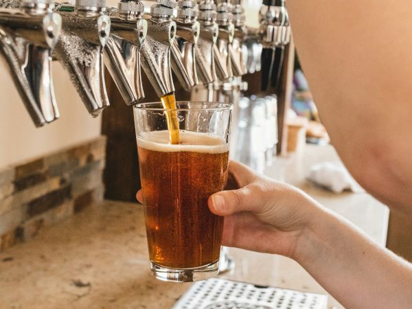 A hand pours beer from a draft tap into a clear glass, with rows of other taps in the background.