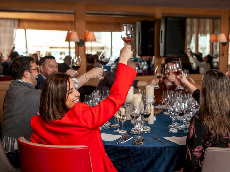 A group of people toasting with wine glasses around a round dining table in a cozy restaurant.