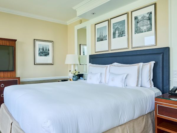 A neatly made hotel room with a large bed, nightstands, and framed pictures on the wall. It appears cozy and well-organized.