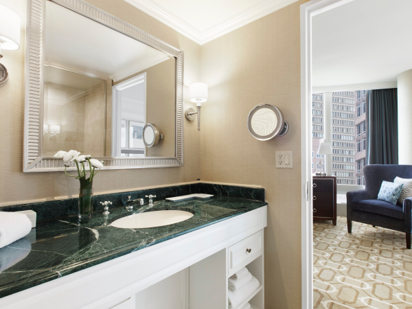 An elegant bathroom leading to a bedroom with a view of a cityscape.