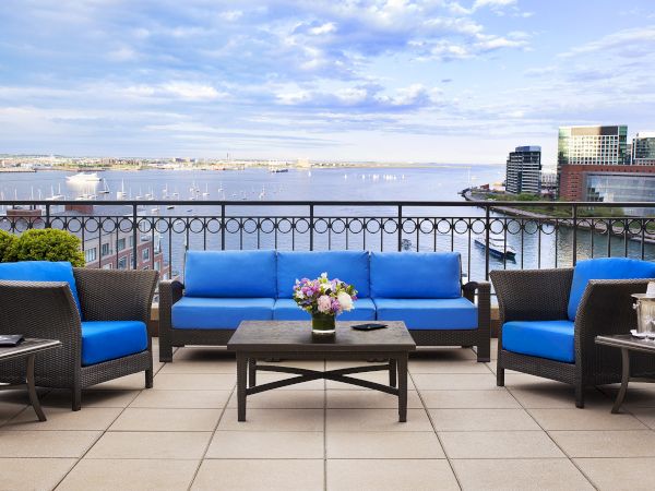 A balcony with blue sofas, table, and flowers overlooking a waterfront view.