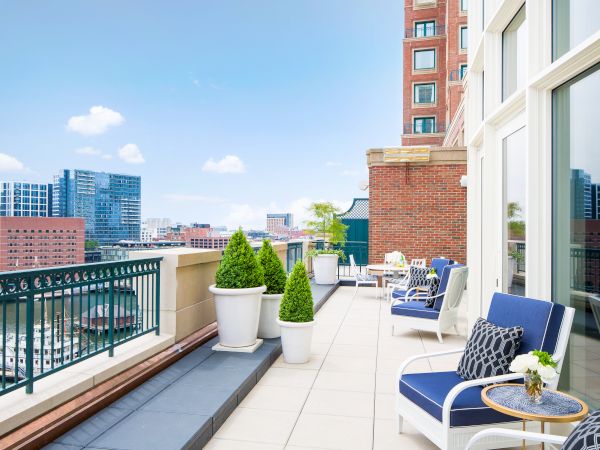 A sunny balcony with seating, plants, and a city view.