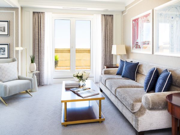 A well-lit living space with a sofa, chairs, table, and doors to a balcony.