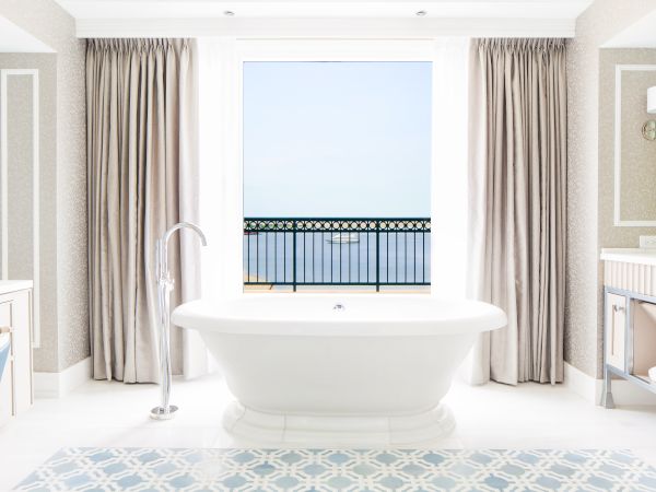 Bright bathroom with a freestanding tub, window view, and patterned floor.