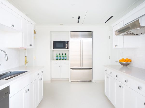 Modern white kitchen with appliances, cabinets, and fruit on the counter.