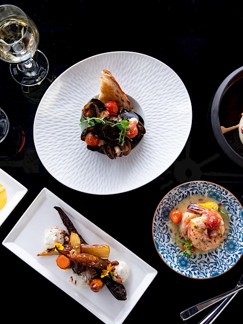 A top-down view of an elegant dining spread with assorted plated dishes, wine glasses, and utensils on a dark table.