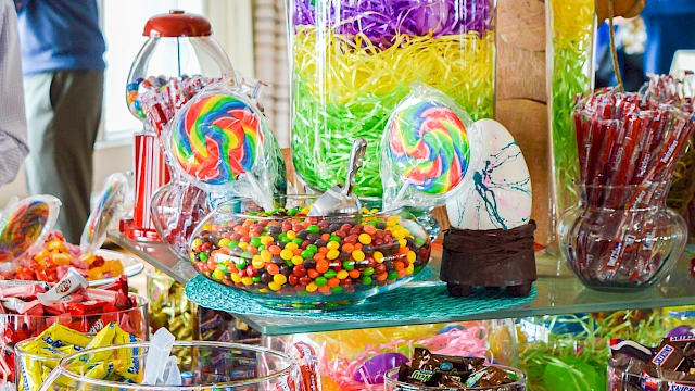 A festive Easter candy display with colorful treats, lollipops, jellybeans, and chocolate eggs arranged around a teal &ldquo;EASTER&rdquo; sign, candy-coated delight.