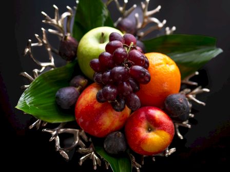 An assortment of fresh fruits with leaves, artistically arranged on a dark background.