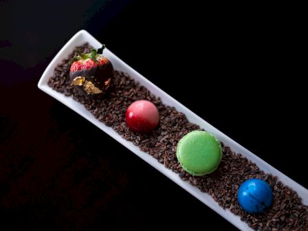 A dessert with a chocolate-dipped strawberry and colorful macarons on chocolate sprink