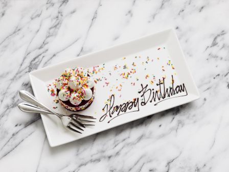 A birthday cupcake with sprinkles on a plate saying "Happy Birthday".
