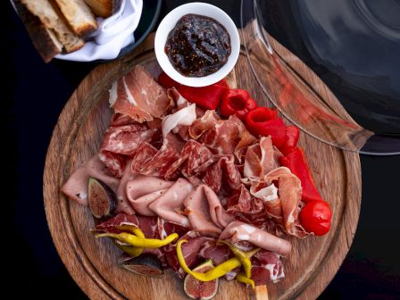 Charcuterie board with cured meats, peppers, tomatoes, dip, and bread