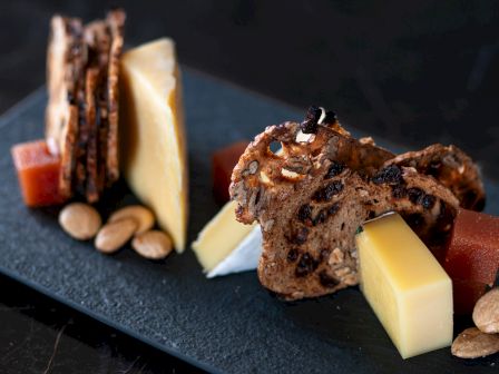 Gourmet cheese and crackers, some nuts, and fruit jelly on a slate board