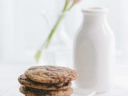Stack of cookies on a plate, a milk bottle, and a pink flower in
