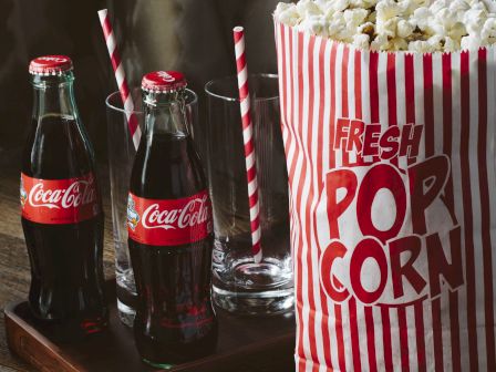 Popcorn in a striped box, two Coca-Cola bottles, candy bars, and