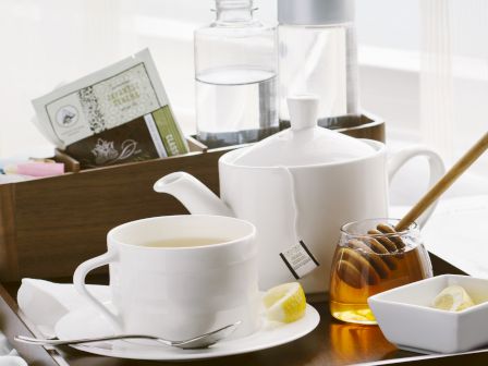 A breakfast tray with cups, a teapot, honey, and a newspaper on