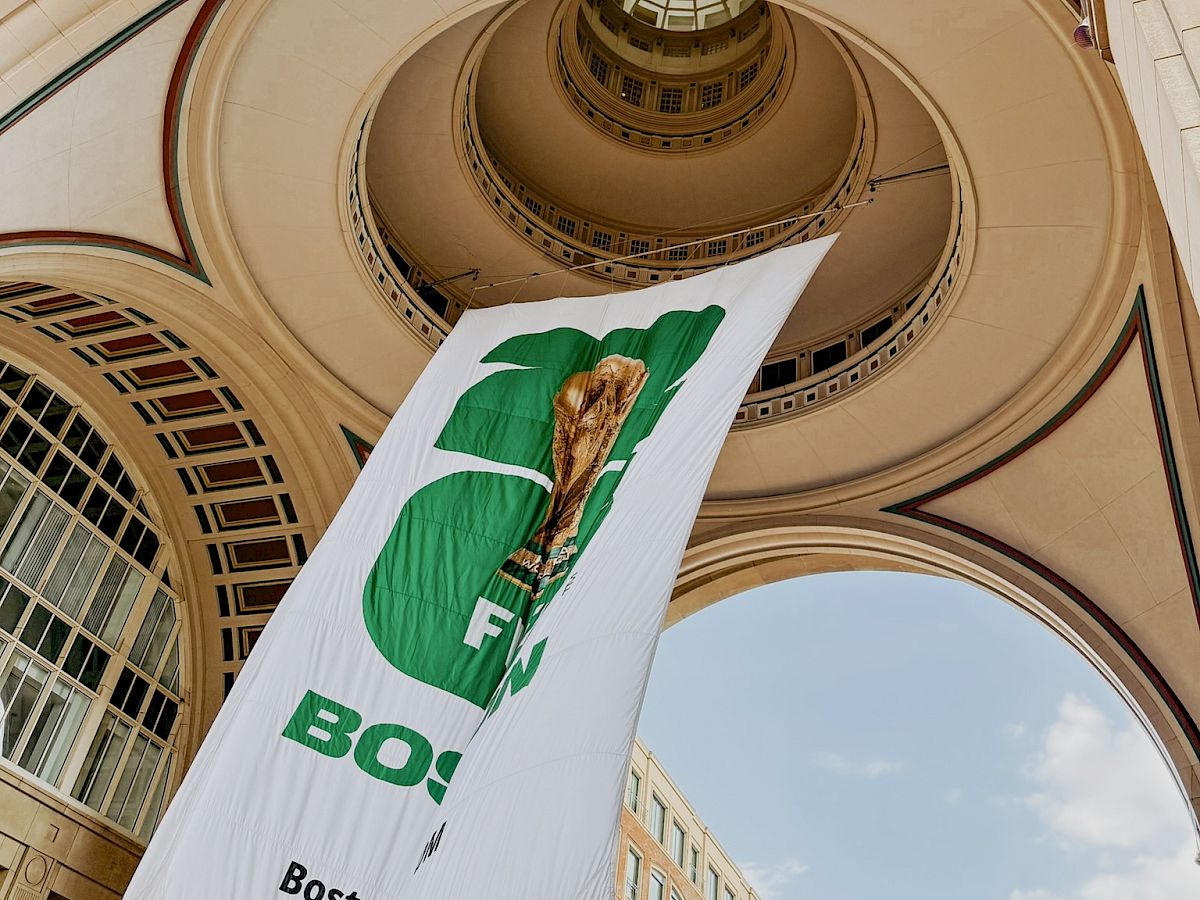 A tall indoor architectural spiral staircase viewed from below, with a hanging banner featuring a green torch and Boston branding.