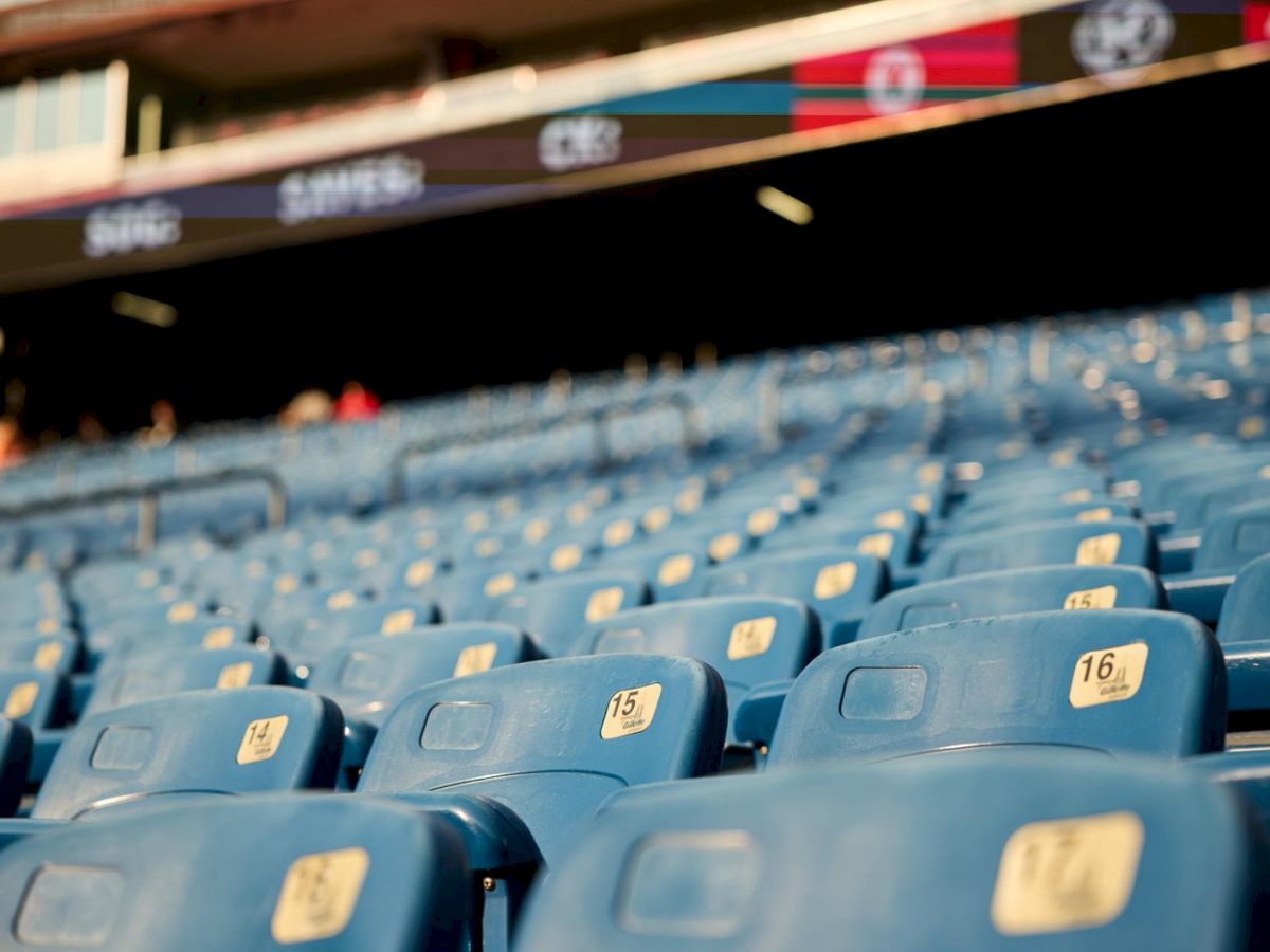 A photo of blue stadium seats in a venue, empty and orderly, with numbered tags on each chair, likely a sports or event stadium ending in a period.