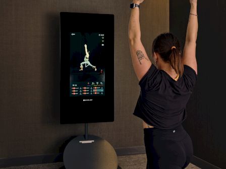 A person does a yoga pose or stretch in a dim-room with a digital screen on the wall, practicing balance and mindfulness.