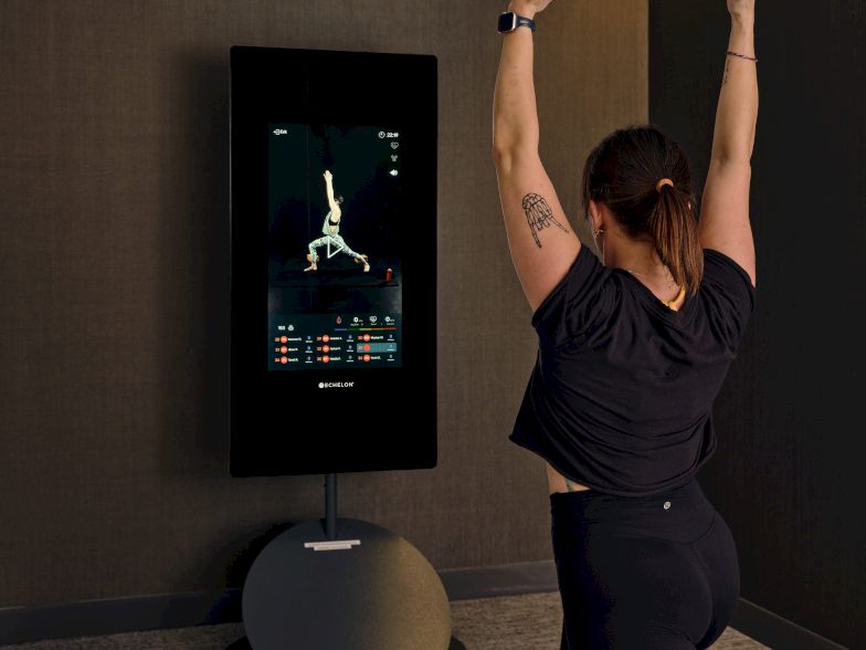 A person does a yoga pose or stretch in a dim-room with a digital screen on the wall, practicing balance and mindfulness.
