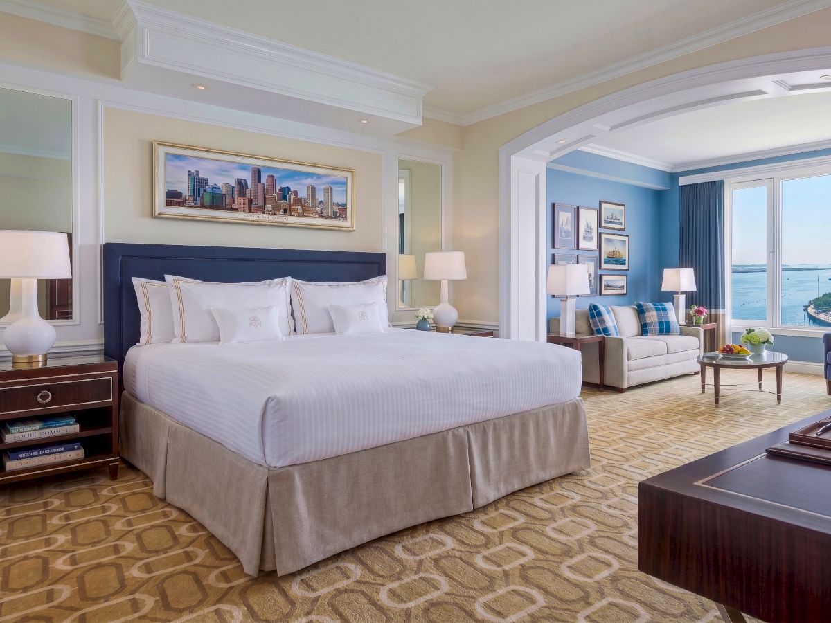A luxurious hotel bedroom with a large bed, bedside lamps, framed art, and a window view over the water.
