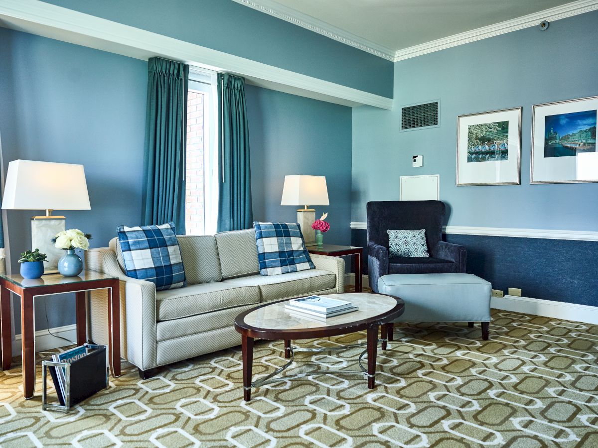 A cozy living room with a blue theme, featuring a sofa, armchair, two lamps, a coffee table, and framed artwork on the walls.