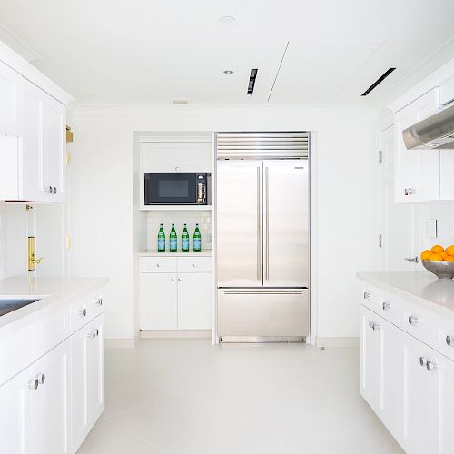 Modern white kitchen with appliances, cabinets, and fruit bowl.