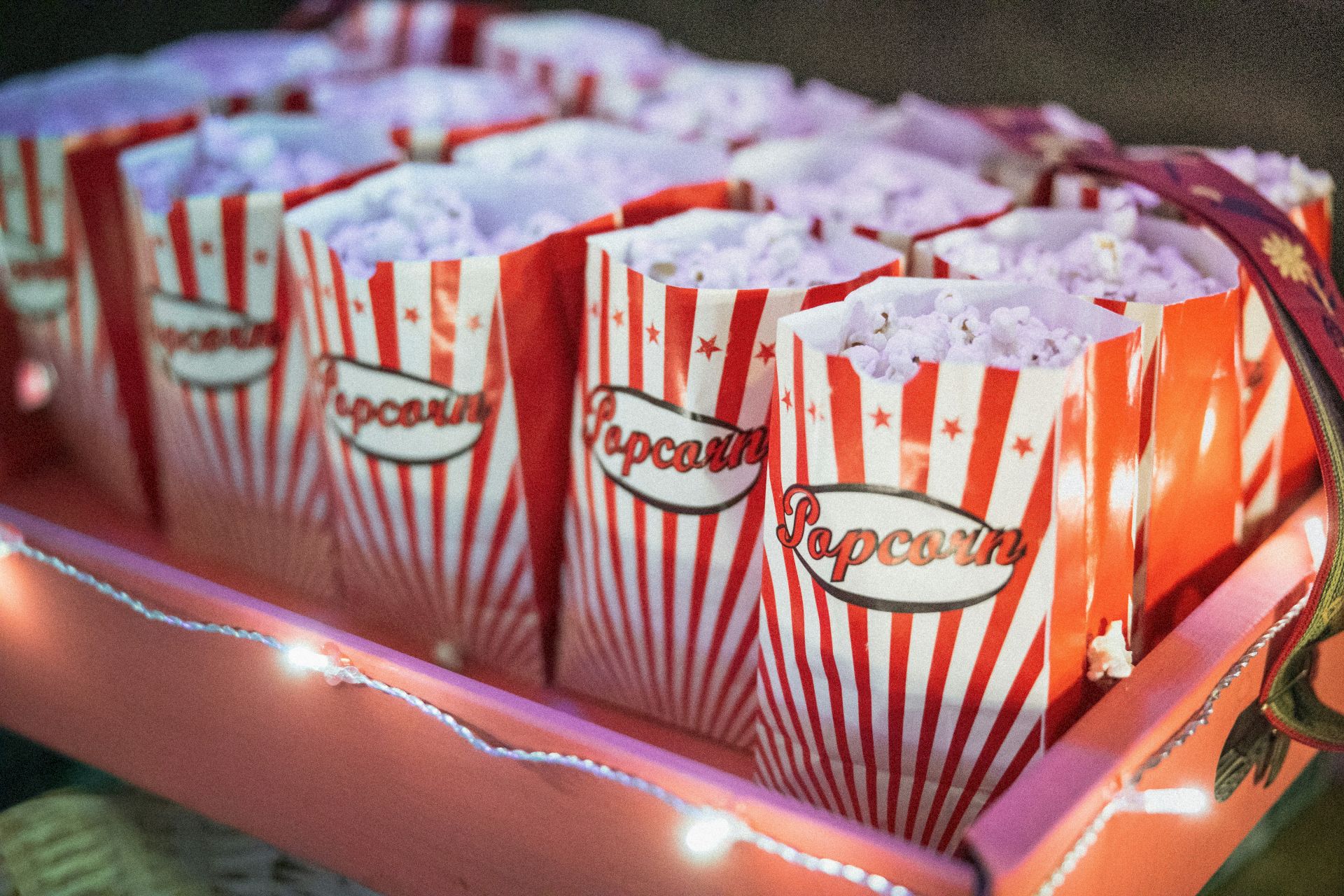 A red-and-white striped popcorn tub with &ldquo;popcorn&rdquo; branding and confetti-like stars, like a snack stand container.