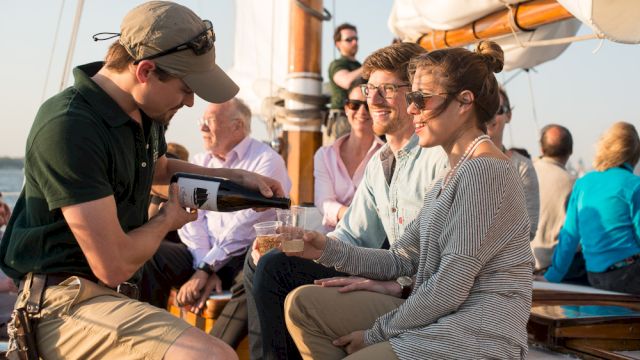 A person is pouring a drink for a woman on a boat with several people enjoying the setting.