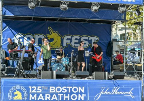 A band performs on stage at the 125th Boston Marathon with the backdrop reading "Fan Fest." John Hancock is one of the sponsors, as seen on signage.
