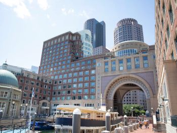 The image shows a cityscape with modern buildings, including an arched structure and domed building, and a waterside walkway.