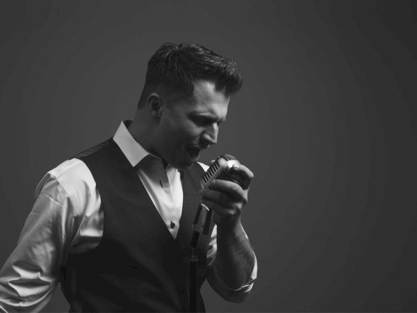 Black and white photo of Rich DiMare who is holding a microphone and singing