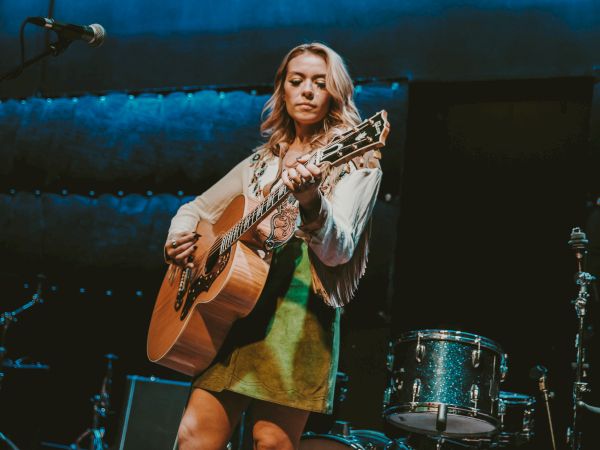Musician Amanda Stewart playing the guitar on stage in front of a band.