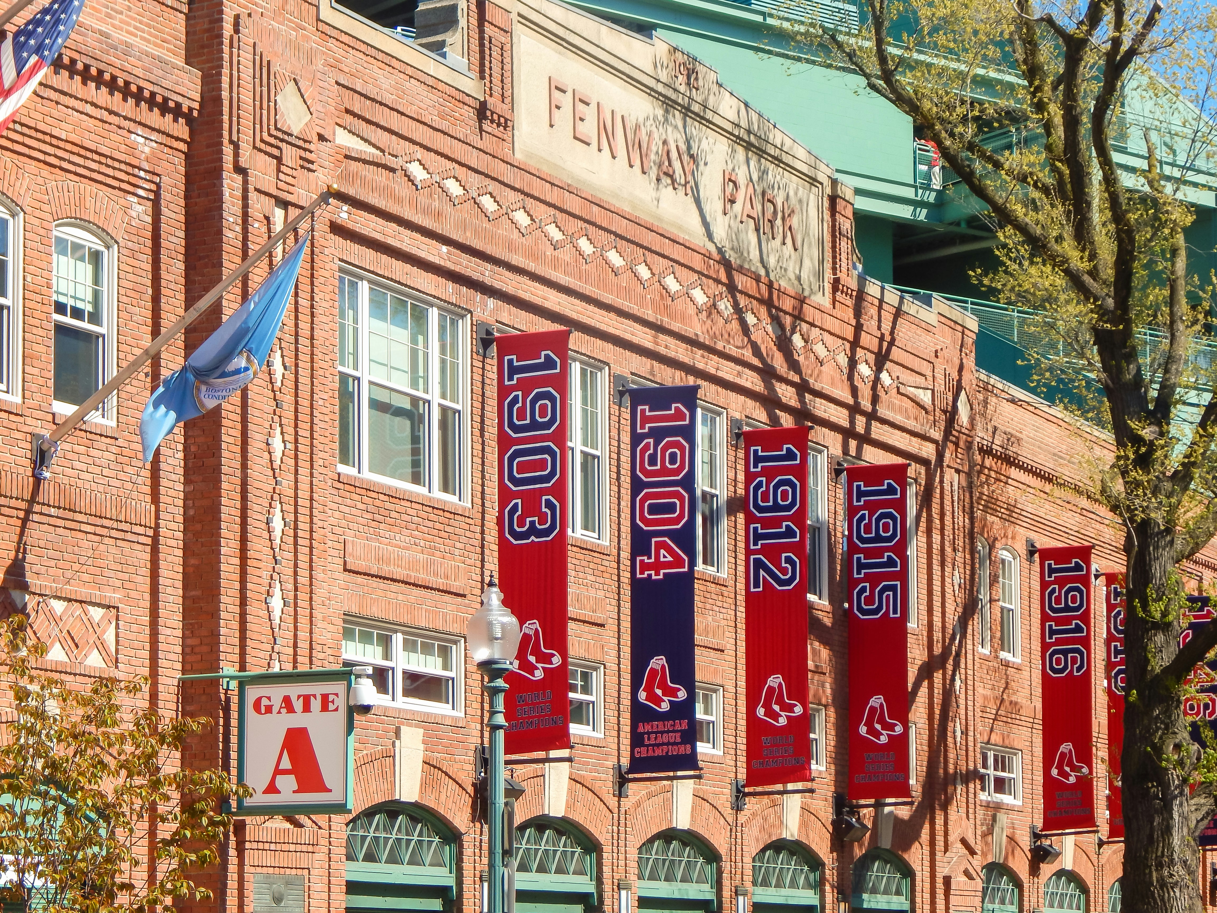 A brick stadium facade with banners showing years from 1903 to 198? hanging along the entrance, flagpoles, and a gate marked &ldquo;Gate A.&rdquo;